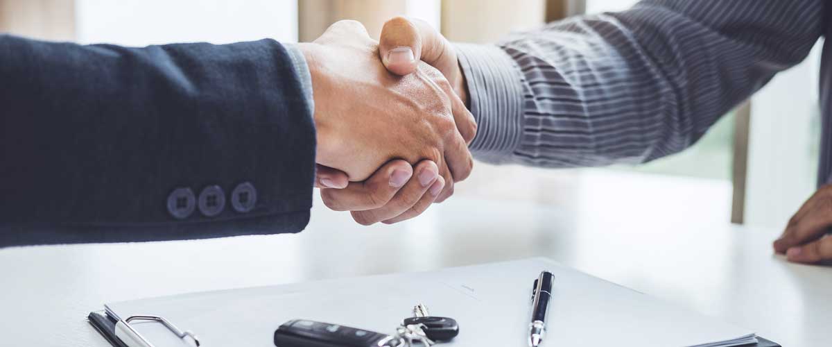 Salesperson and customer shake hands to finalize the contract that they reviewed to finalize the car purchase