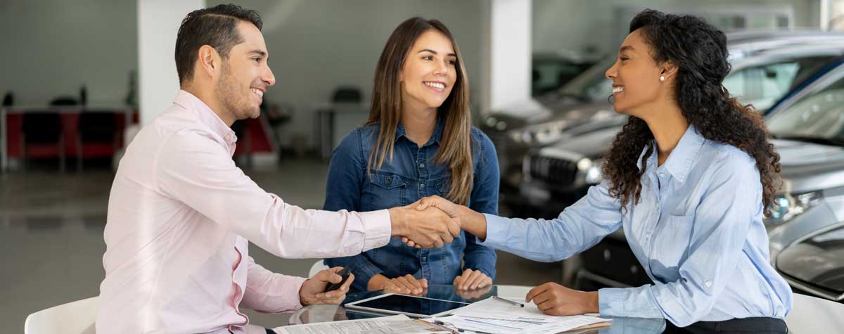 Happy couple signs car purchase shakes their salespersons hand to seal the deal