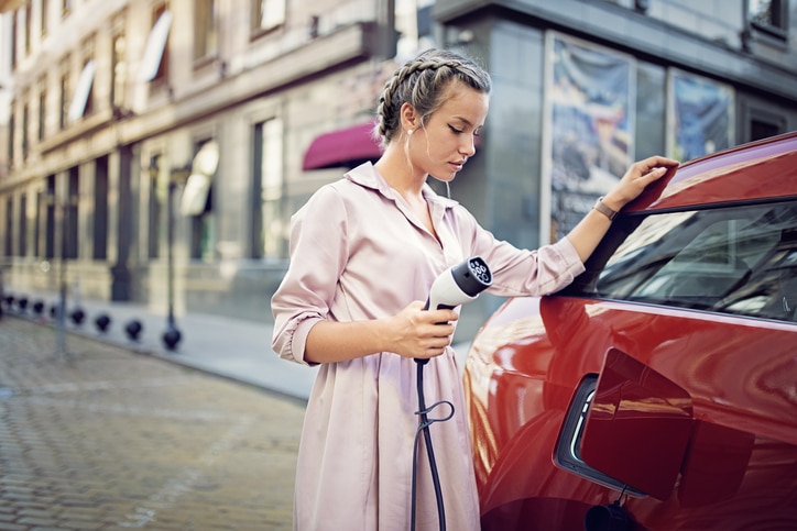 Young woman is charging her electric car in the city