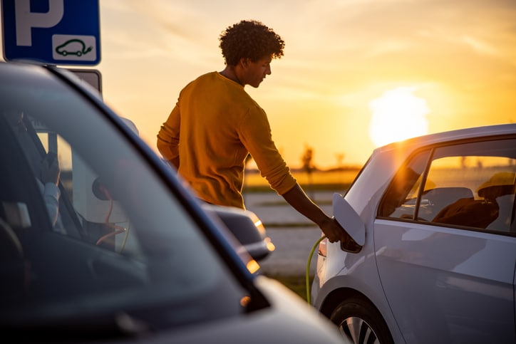 Young man charging his EV with a sunset in the background