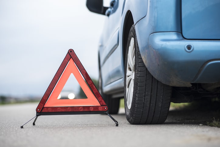 Close up of a warning triangle on the road next to car.