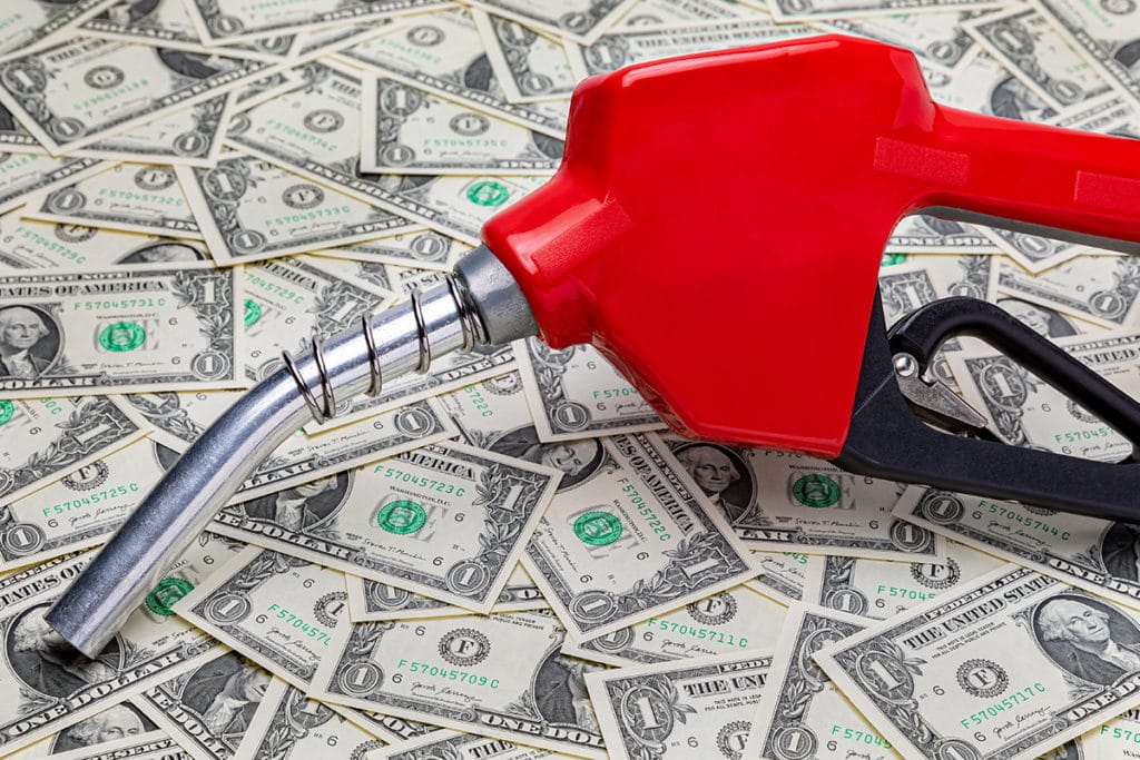 Fuel nozzle on money to represent the need to pay attention to gas milage.