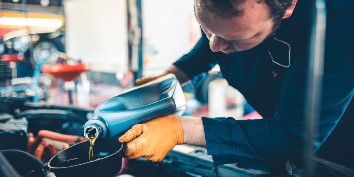 Auto Mechanic working on car - Worker at the auto mechanic shop. Location portrait at the place of work. Oil change on the vehicle.