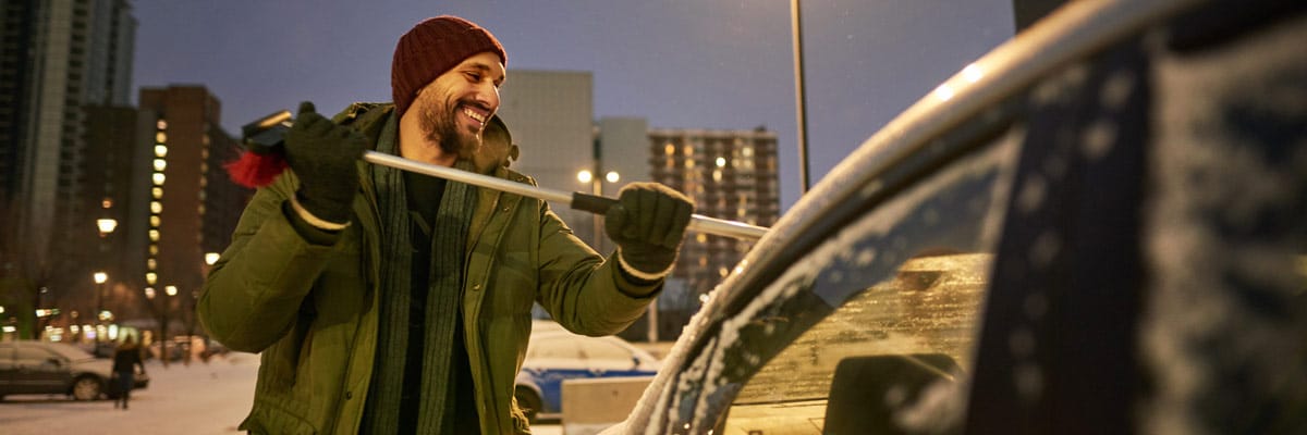 Shot of a man removing snow from his car during cold winters evening.