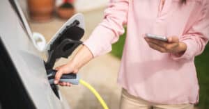 Woman charging electric car and making time adjustment on a smartphone