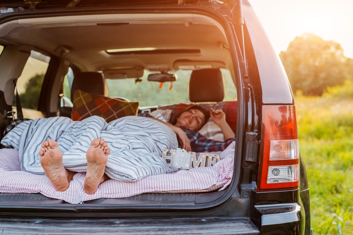 woman sleeps comfortably her car Luggage compartment nature summer under blanket. concept caravanning free travel for weekend. Vacation, tourism, privacy in country, motor home, camping, mobile home.